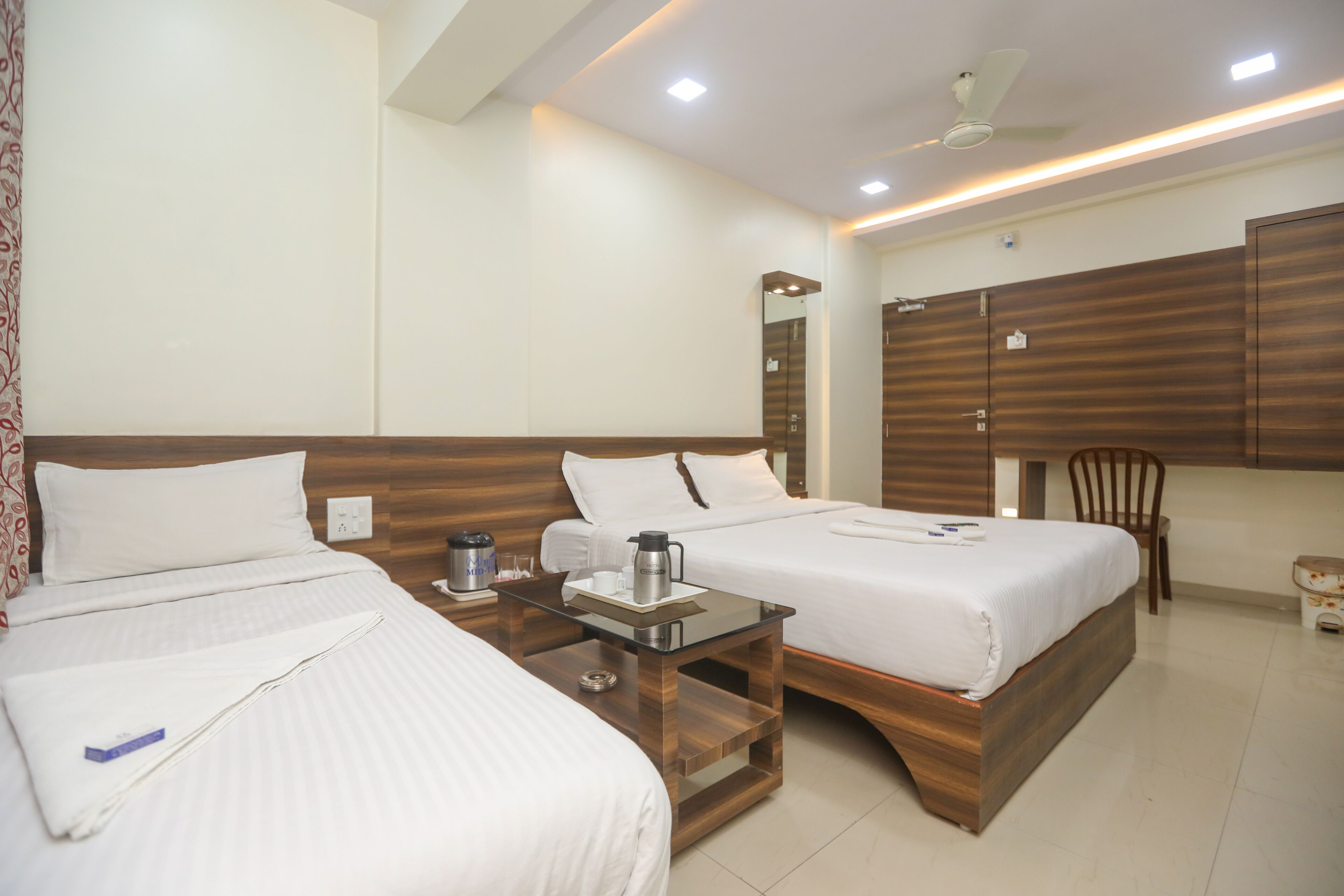 A hotel room with two beds, a wooden headboard, a small table with a kettle and cups, and a wardrobe.