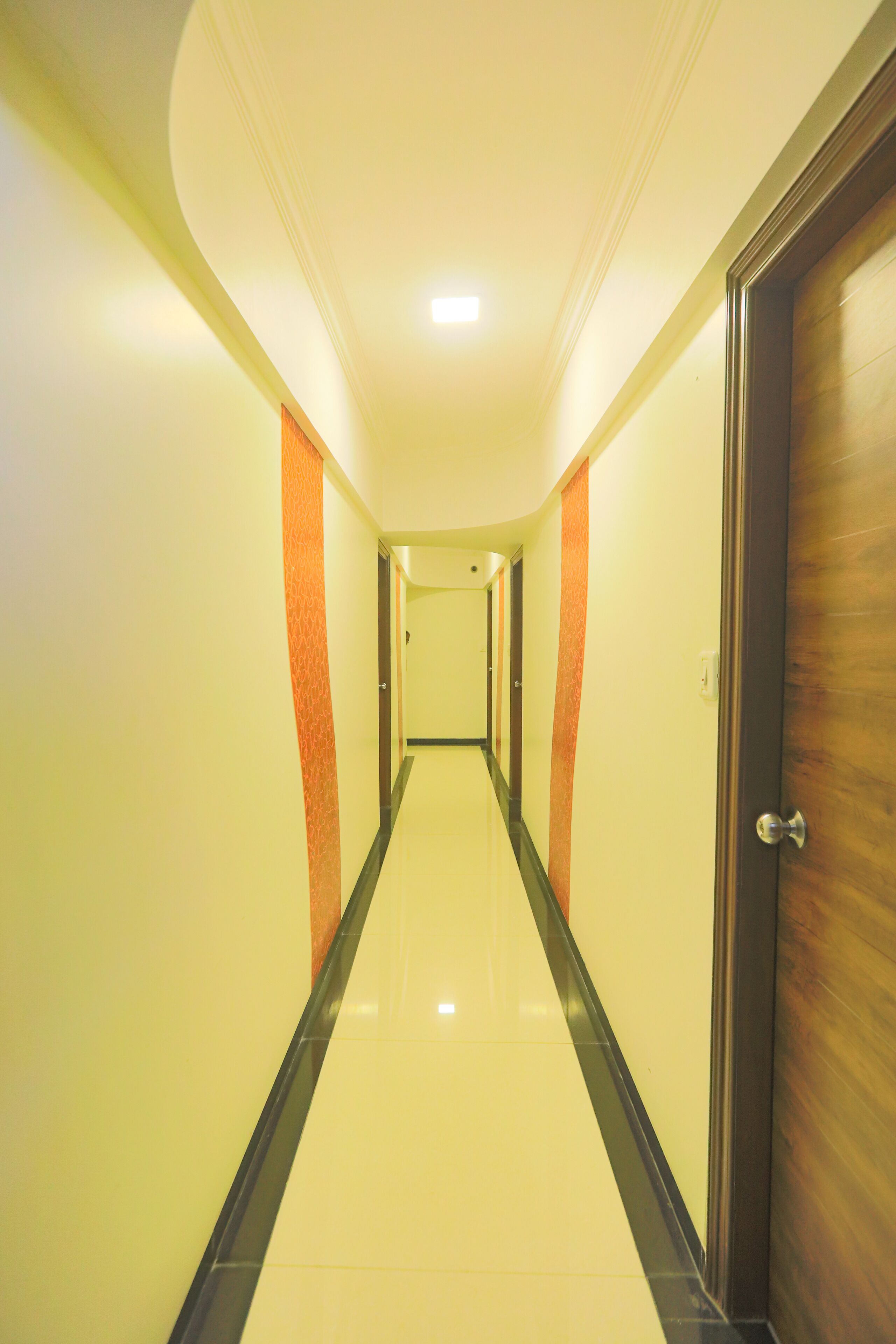 A hotel hallway with a shiny tiled floor, a wooden door on the right, and orange accents on the walls.