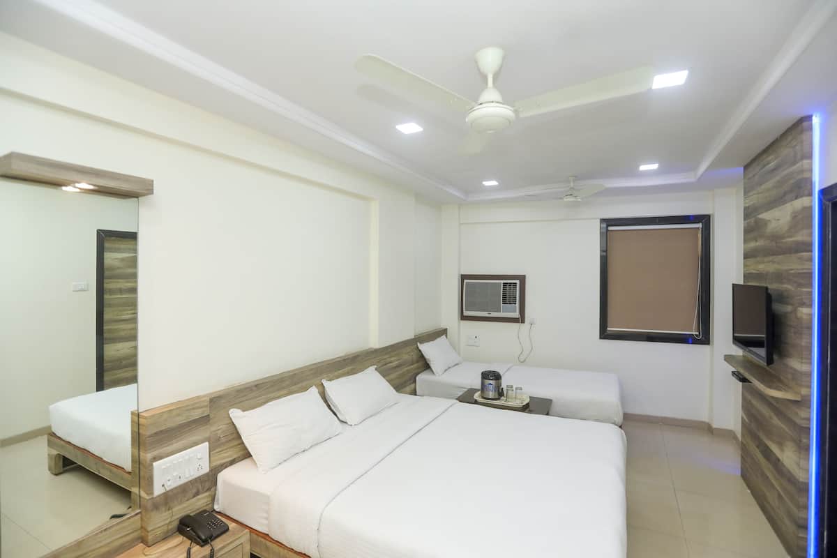 Une chambre d’hôtel avec un grand lit, un plus petit lit, un bureau, un miroir, un ventilateur de plafond et une télévision.
