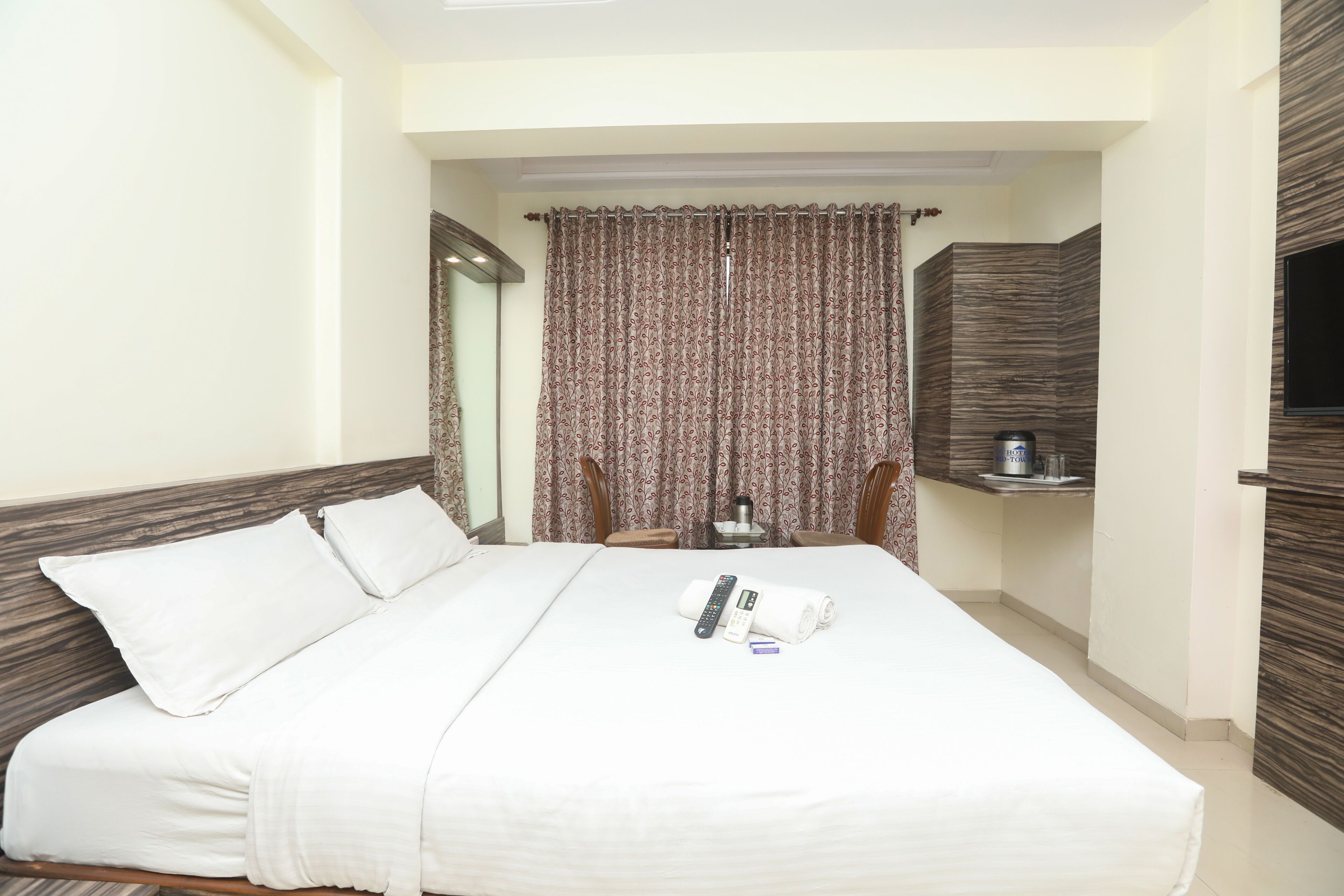 A hotel room with a large bed, a flat-screen TV mounted on the wall, and a small table with a kettle and cups.