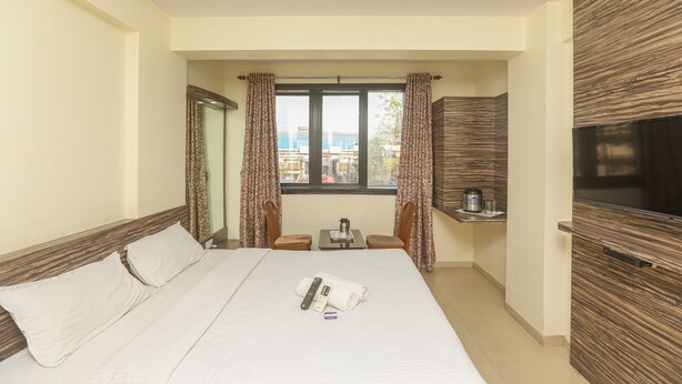 Habitación de hotel con cama, televisor, una mesita con tetera y cortinas.