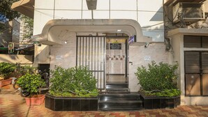 Entrada de un hotel con mostrador de recepción, una escalera que conduce al acceso y plantas en la base.