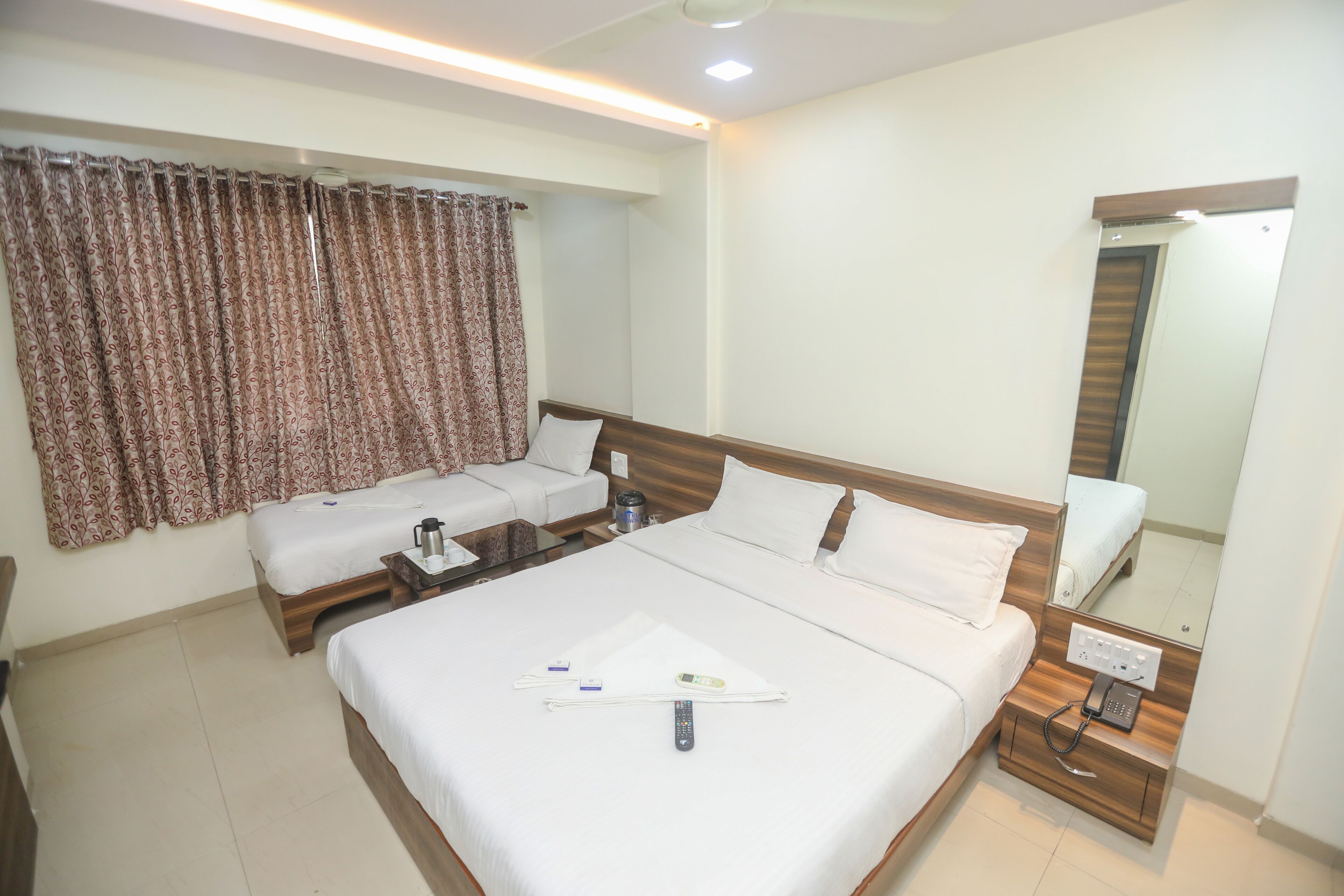 Habitación de hotel con una cama grande, un sofá más pequeño, una mesita de noche con lámpara y un espejo.
