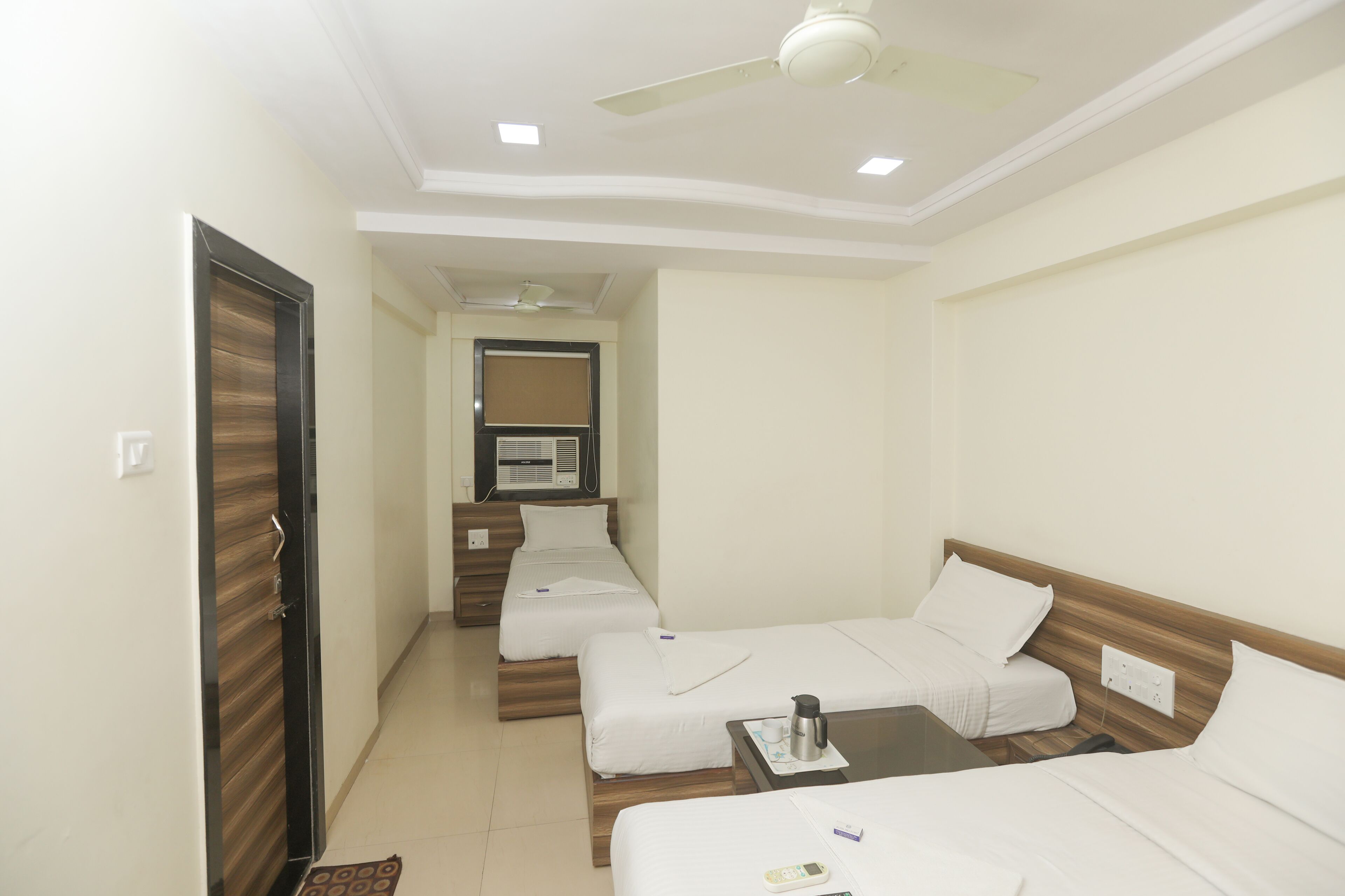 A hotel room with two single beds, a wooden headboard, a small table with a remote control, and a ceiling fan.