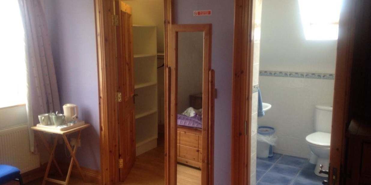 A narrow hallway leading to a bathroom with a toilet and sink. There is a small table with cups and a bottle on the left.