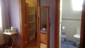 A narrow hallway leading to a bathroom with a toilet and sink. There is a small table with cups and a bottle on the left.