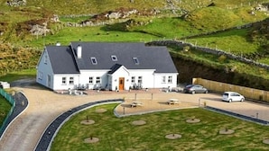 A white building with a grey roof, surrounded by a landscaped area with small trees and a paved driveway. - Slieve League House B&B (Carrick)