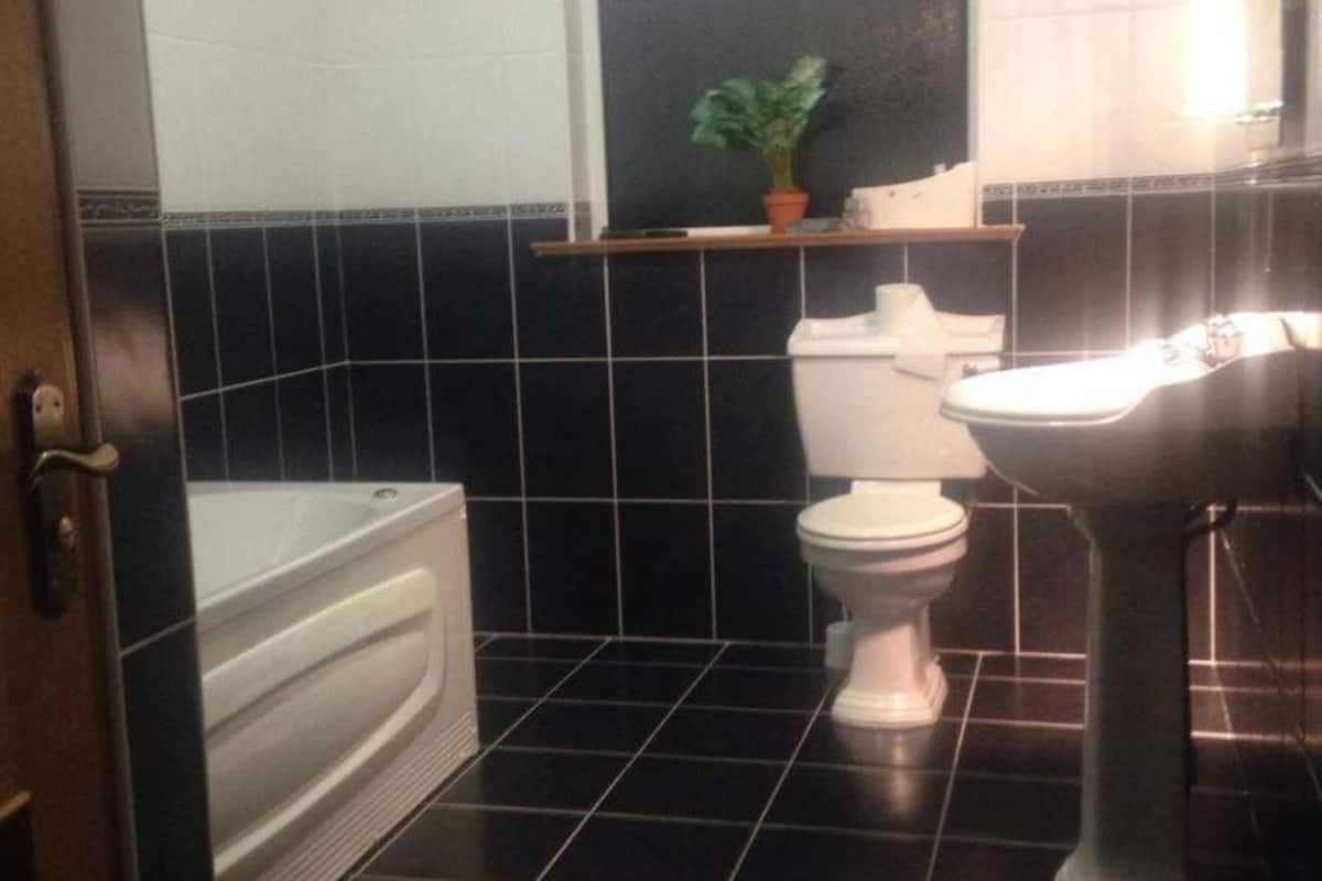 Un baño con bañera, inodoro y lavamanos, con paredes de azulejos negros y una puerta de madera.