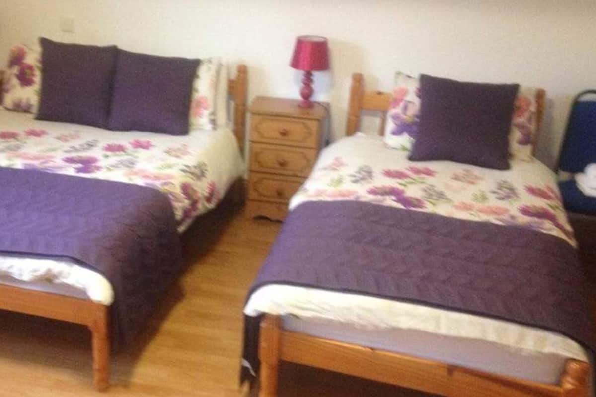 Dos camas individuales con cabeceros de madera y ropa de cama floral, cada una con una mesita de noche y lámpara.