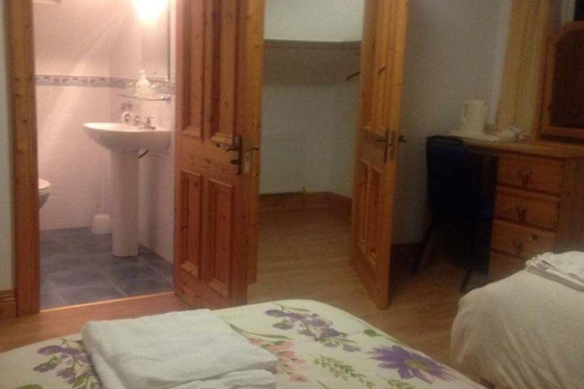 Un dormitorio con cama, cómoda, televisor y puerta abierta que da a un baño.