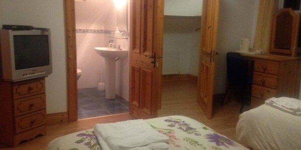 A bedroom with a bed, a dresser, a television, and an open door leading to a bathroom.