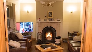 A cozy living room with leather sofas, a wooden coffee table, a fireplace, and a television. - Slieve League House B&B (Carrick)