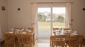 A dining area with a table set for four, wooden chairs, and a view of a rural landscape through a glass door. - Slieve League House B&B (Carrick)