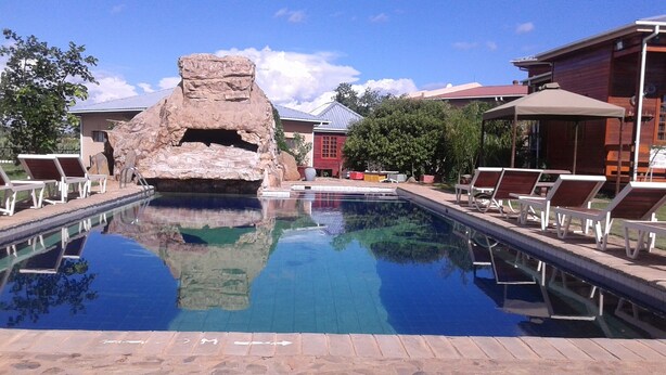 A swimming pool with lounge chairs, a rock formation, and a building with a red facade. - Adansonia Hotel (Francistown)