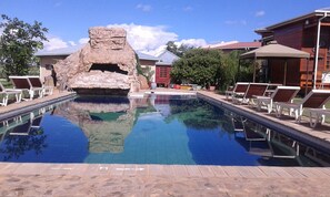 Una piscina con sillas de descanso, una formación rocosa y un edificio con fachada roja.