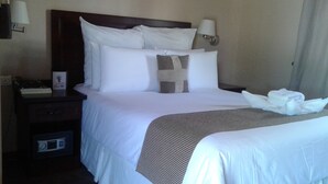 A hotel room with a large bed, two pillows, a bedside table with a lamp, a nightstand with a telephone, and a folded towel on the bed. - Adansonia Hotel (Francistown)