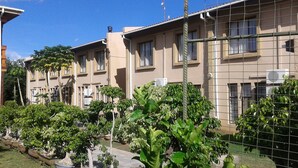A row of beige residential buildings with multiple windows, some with air conditioning units. There are various potted plants and trees in the foreground. - Adansonia Hotel (Francistown)