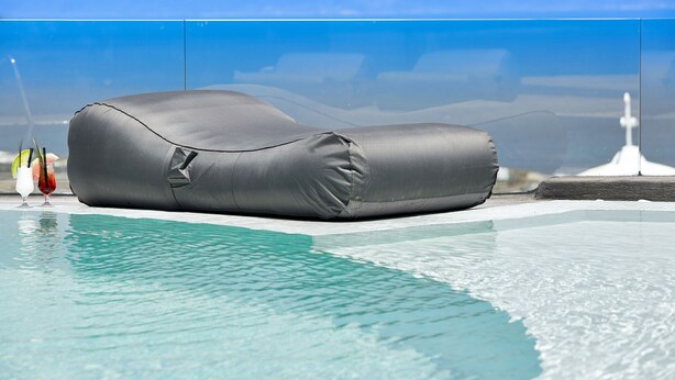 A poolside lounge chair with a water-resistant cover, positioned near a pool with clear blue water. - Aperanto Suites (Santorini)