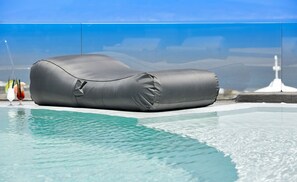 A poolside lounge chair with a water-resistant cover, positioned near a pool with clear blue water. - Aperanto Suites (Santorini)