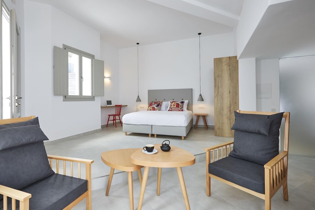 A modern bedroom with a bed, two chairs, a small table, and a window.