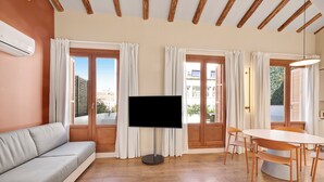 Un salon comprenant un canapé, un téléviseur, une table à manger, des chaises et de grandes fenêtres avec des rideaux.