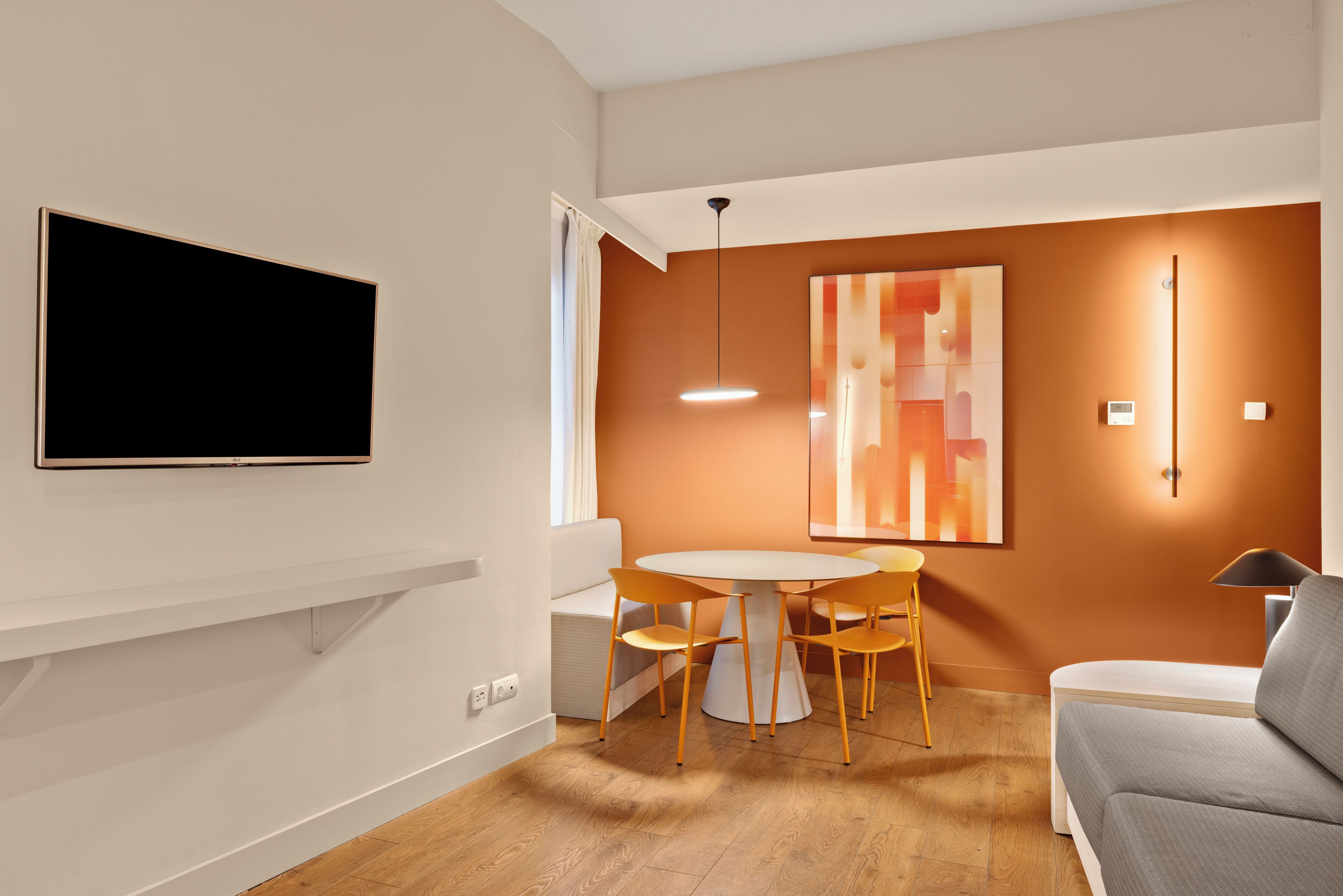 A modern living room with a flat-screen TV, a round dining table with chairs, a sofa, and a large abstract painting on the wall.