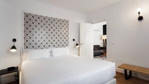 Une chambre d’hôtel moderne avec un grand lit, une table de chevet, un banc et une tête de lit à motifs.