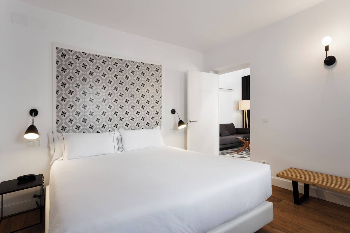 Una habitación de hotel moderna con una cama grande, una mesita de noche, un banco y un cabecero estampado.