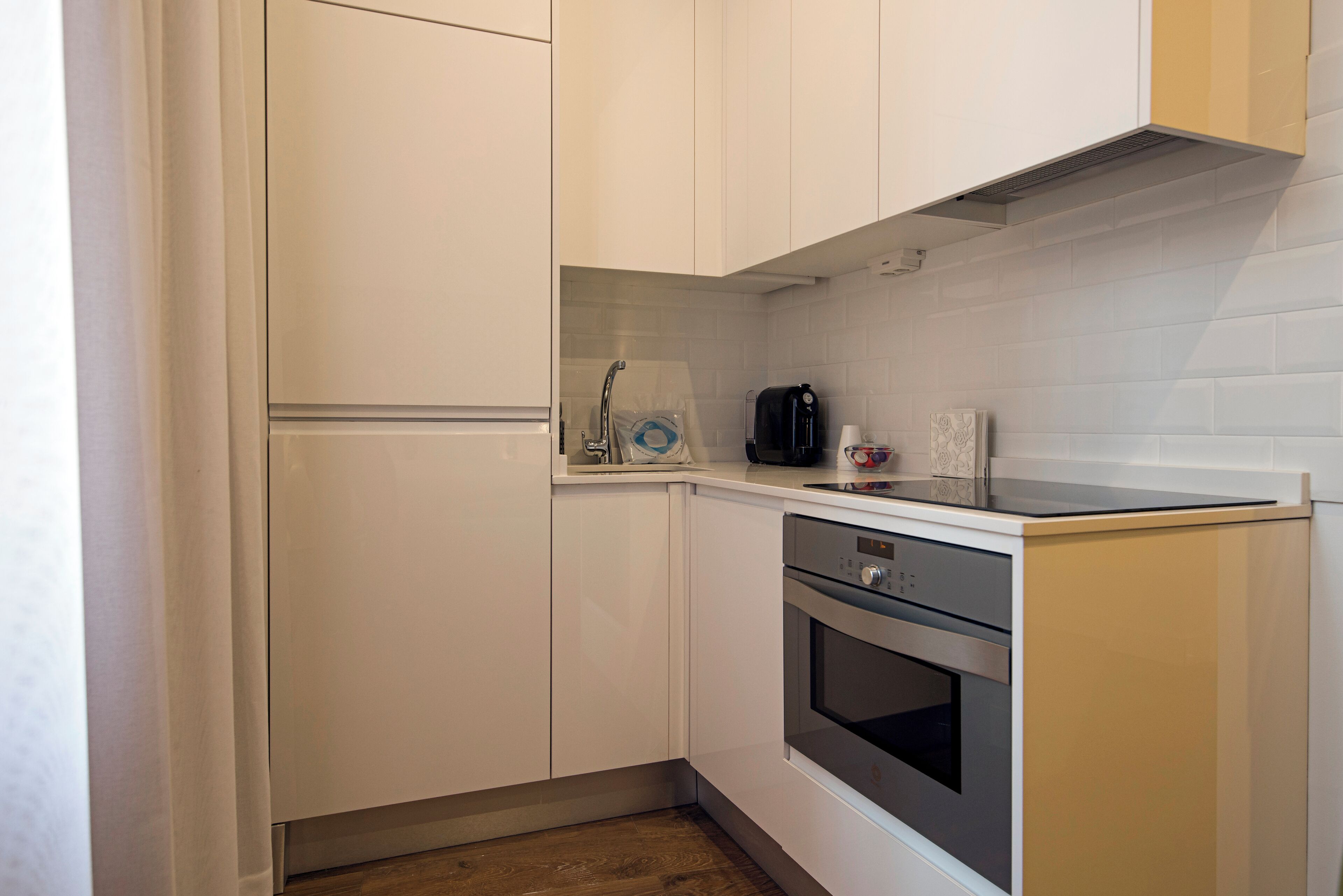 A compact kitchen with white cabinetry, a built-in oven, and a coffee maker.