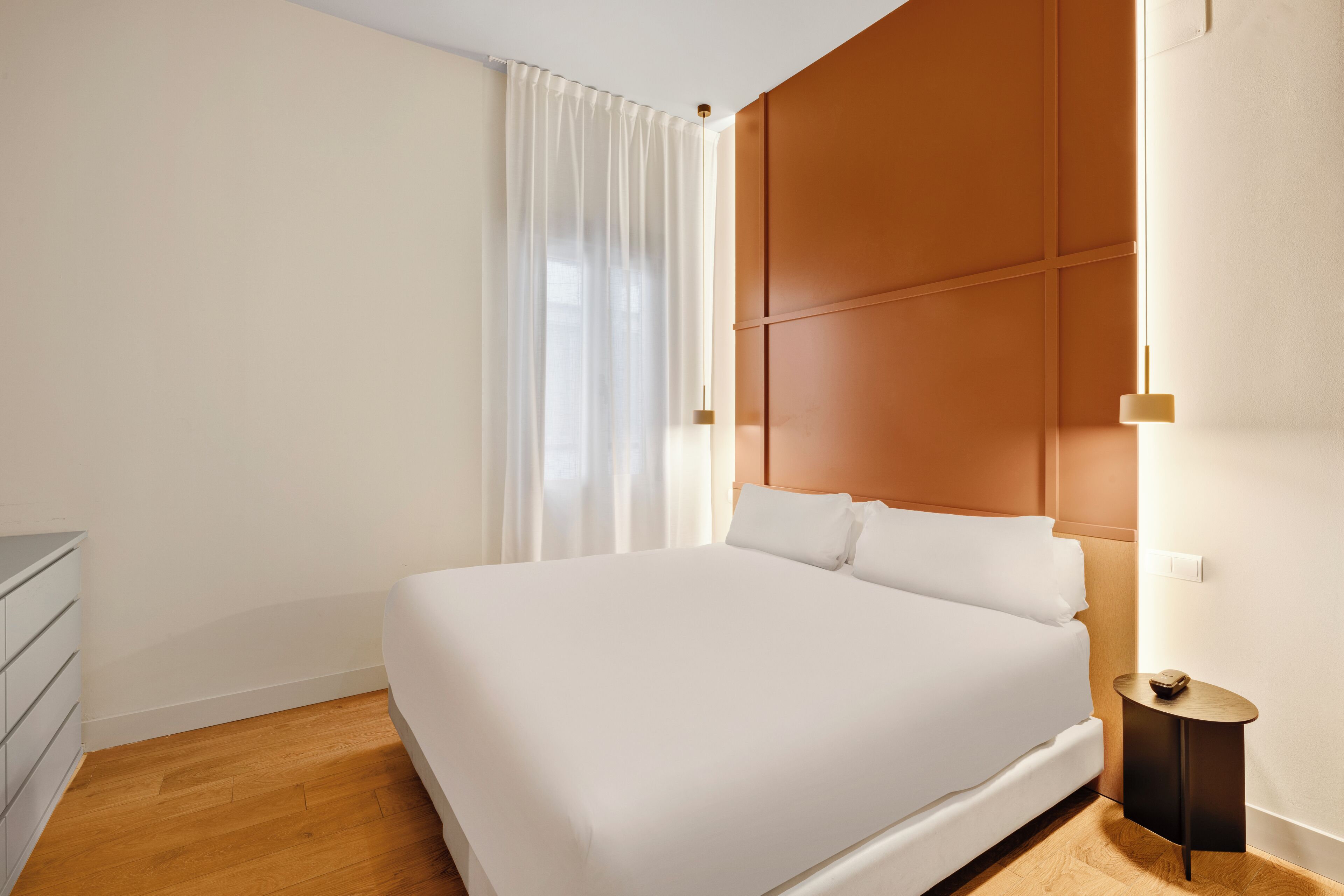 A neatly arranged hotel room with a large bed, a bedside table, a dresser, and a window with curtains.