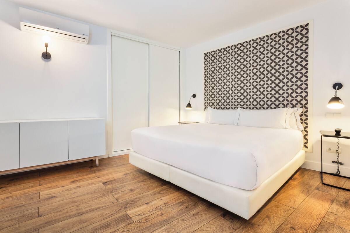Un dormitorio con una cama blanca, suelo de madera, pared estampada y un armario.
