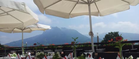 A table set for dining with white tablecloths, red napkins, and glassware, overlooking a mountainous landscape.