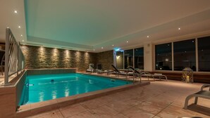 A swimming pool with a stone wall backdrop, lounge chairs, and a view of the night sky. - Hotel Kuehbergalp (Blaichach)