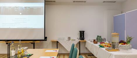 Una sala de conferencias con una mesa larga, sillas, una pantalla de proyector y una mesa de buffet con comida y bebidas.