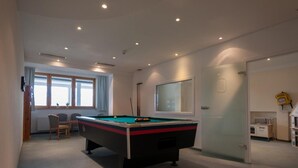 Una mesa de billar en una habitación con ventana, puerta y radiador.