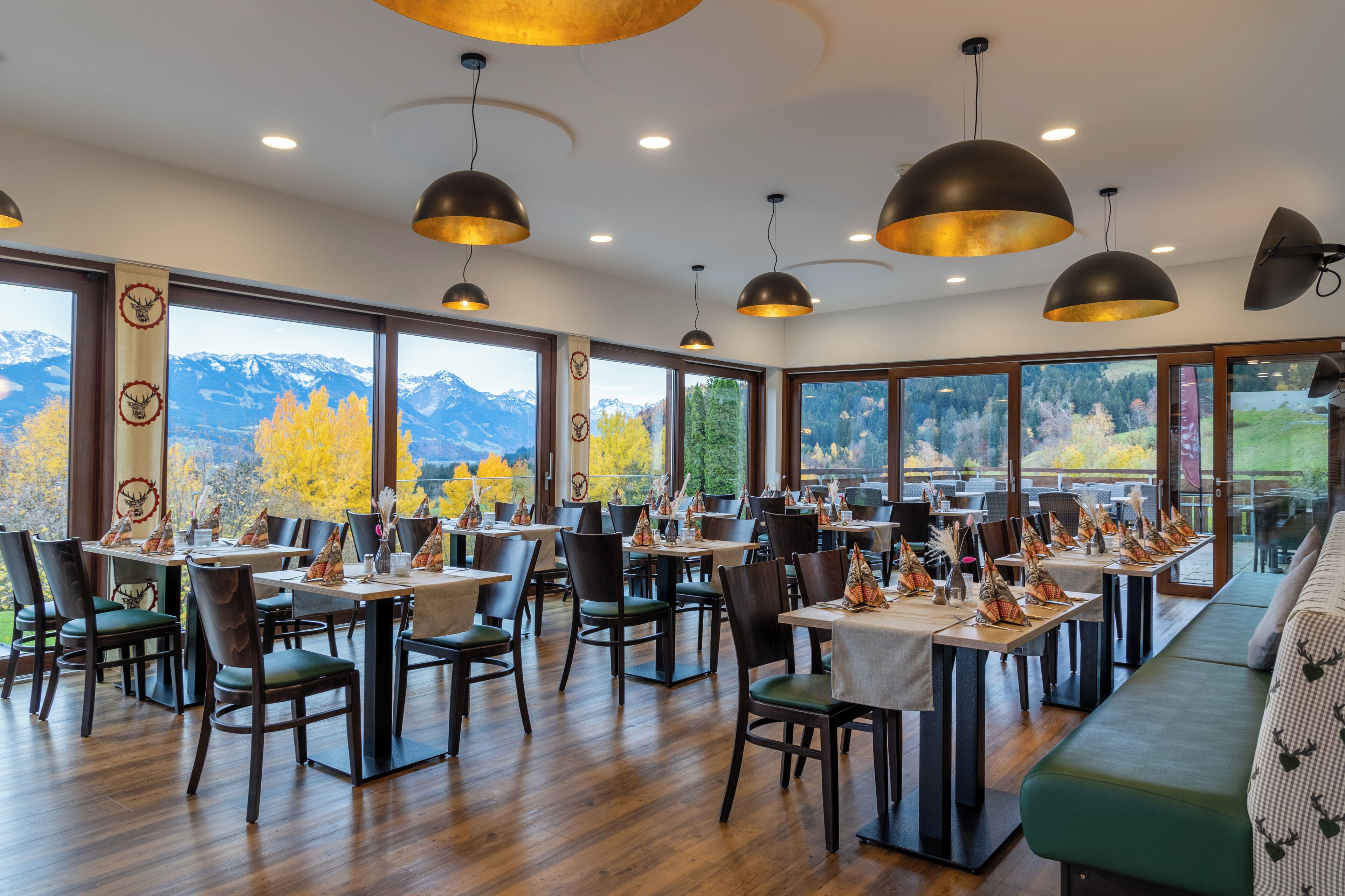 A restaurant with multiple tables and chairs, large windows with mountain views, and pendant lighting.