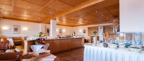 A spacious dining area with wooden ceiling beams, a buffet table with various food items, and a seating area with a bench and baskets.