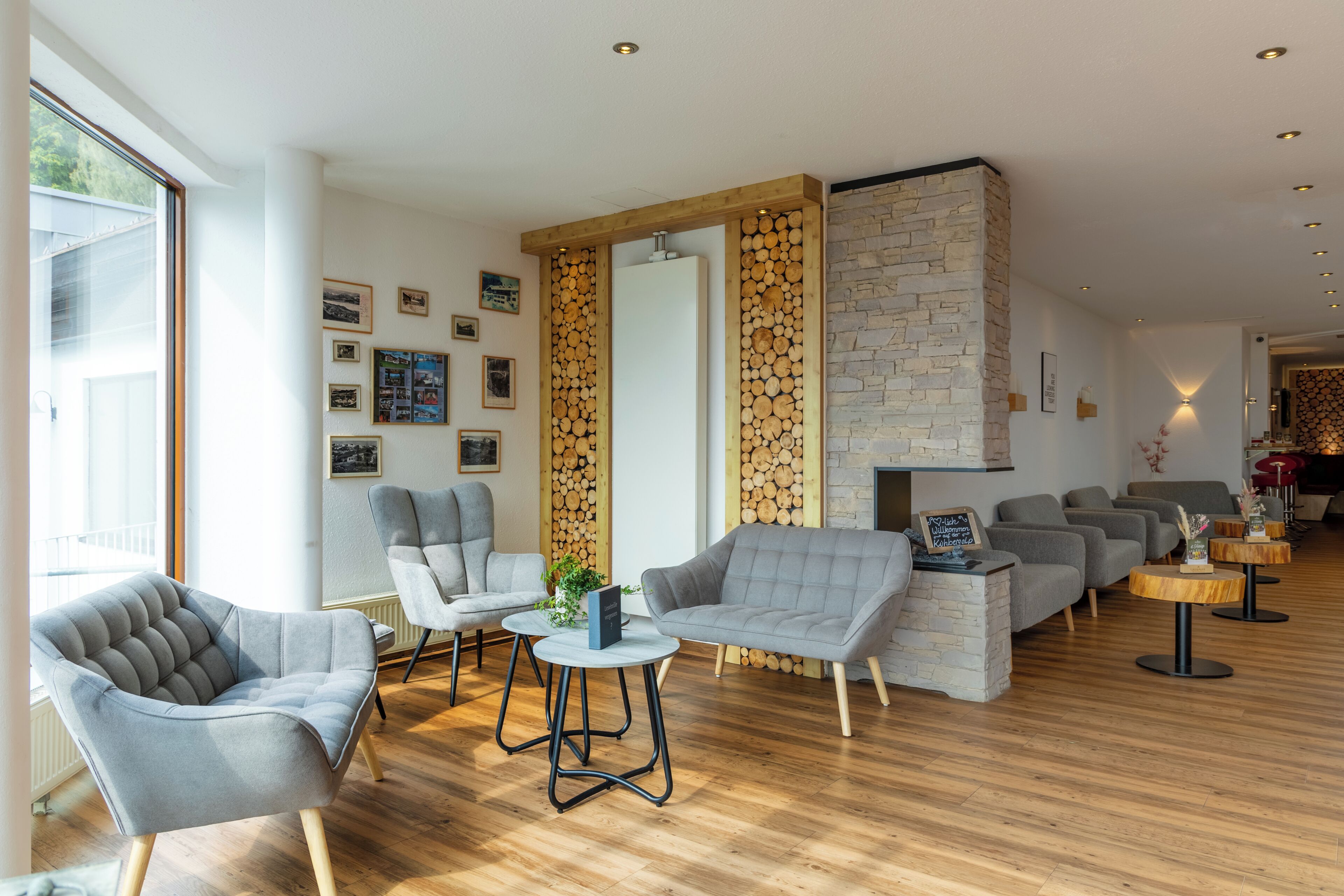 Un área de estar moderna con sillones tapizados en gris, piso de madera y chimenea de piedra.