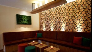 Un interior moderno con un banco de madera, un sofá con cojines verde y rojo, y una pared decorada con leña apilada.