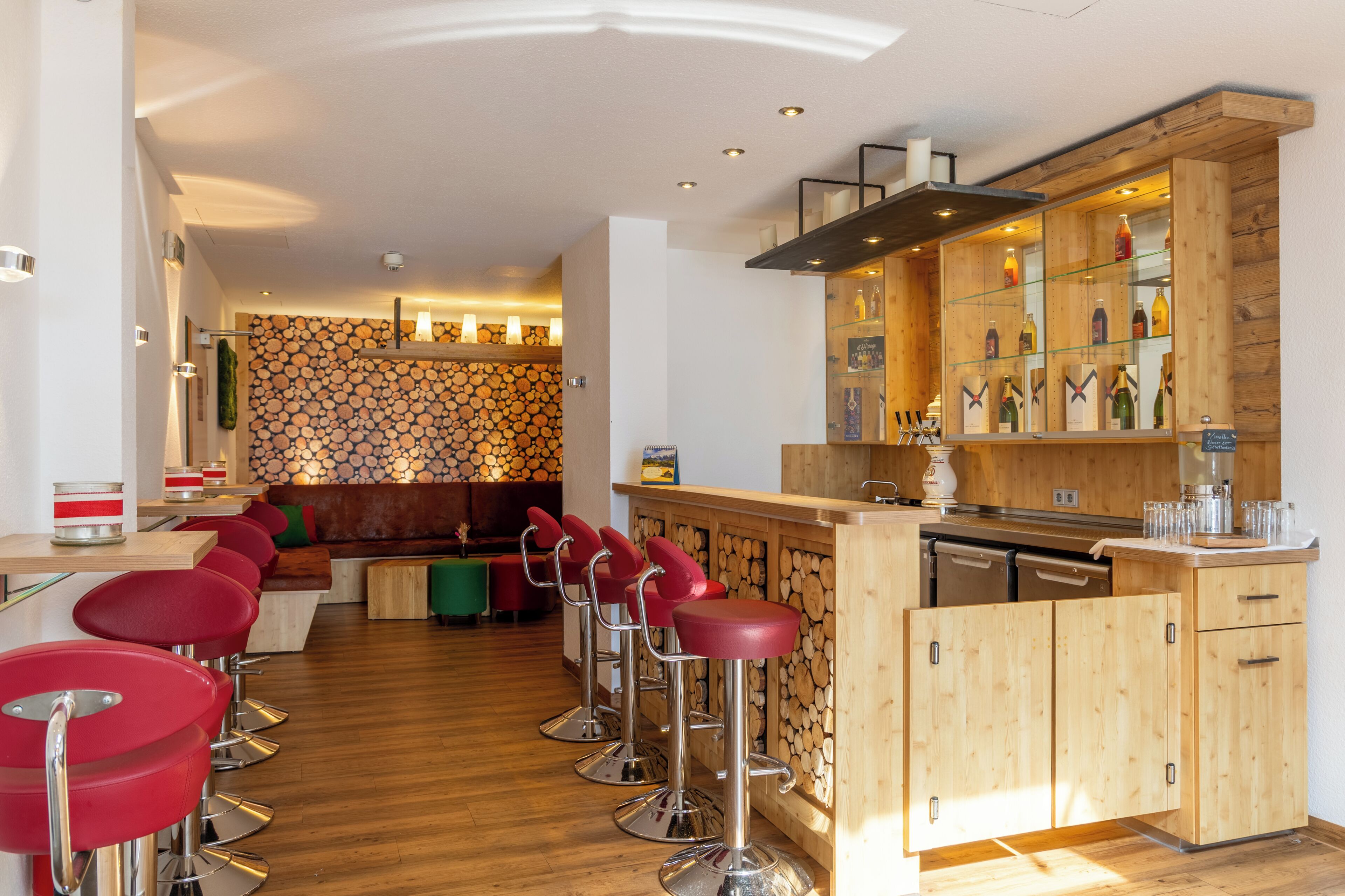 Eine moderne Bar mit Holzelementen, roten Barhocker und einer Auswahl an Getränken.