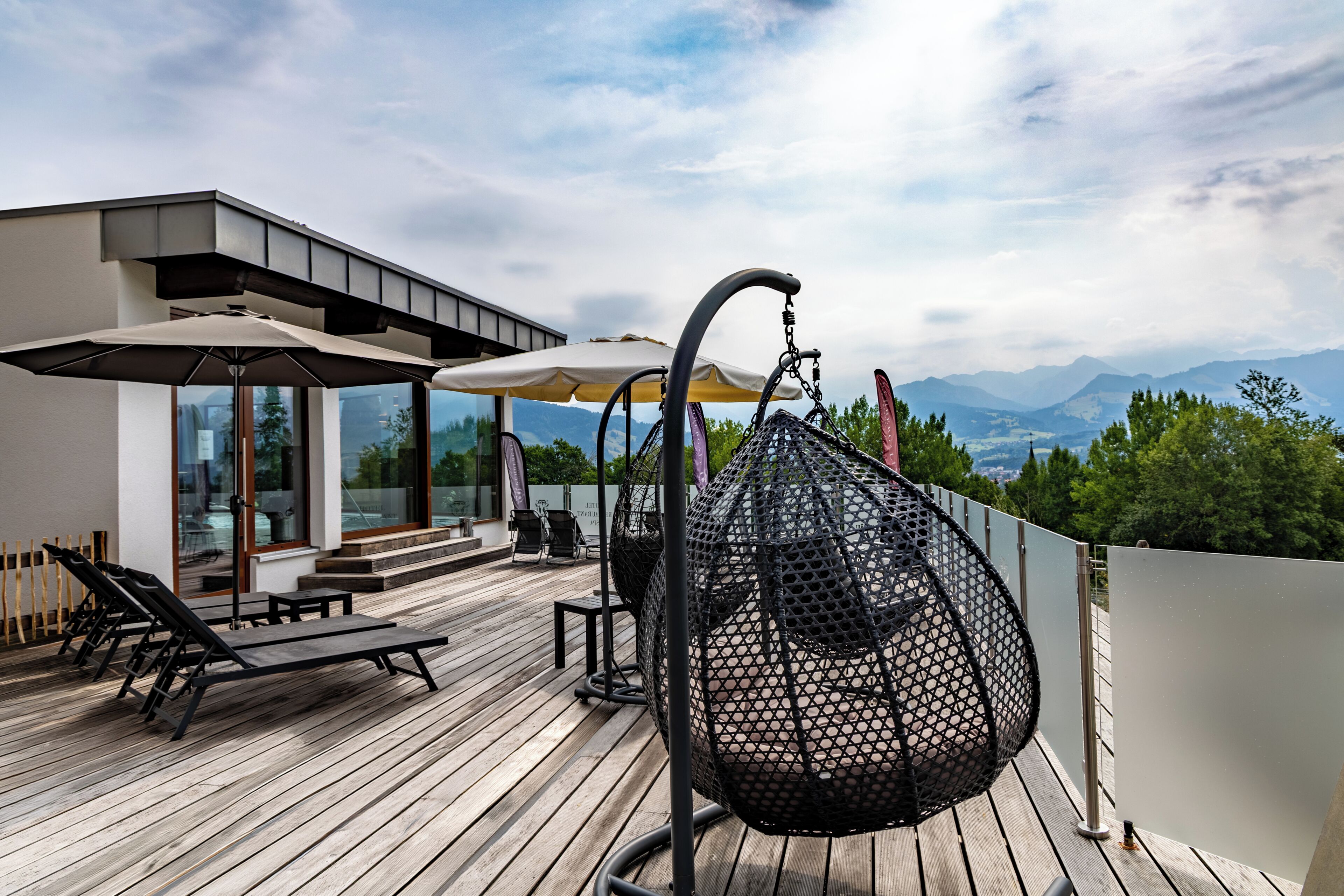 A wooden deck with outdoor seating, a hanging chair, and a view of mountains.
