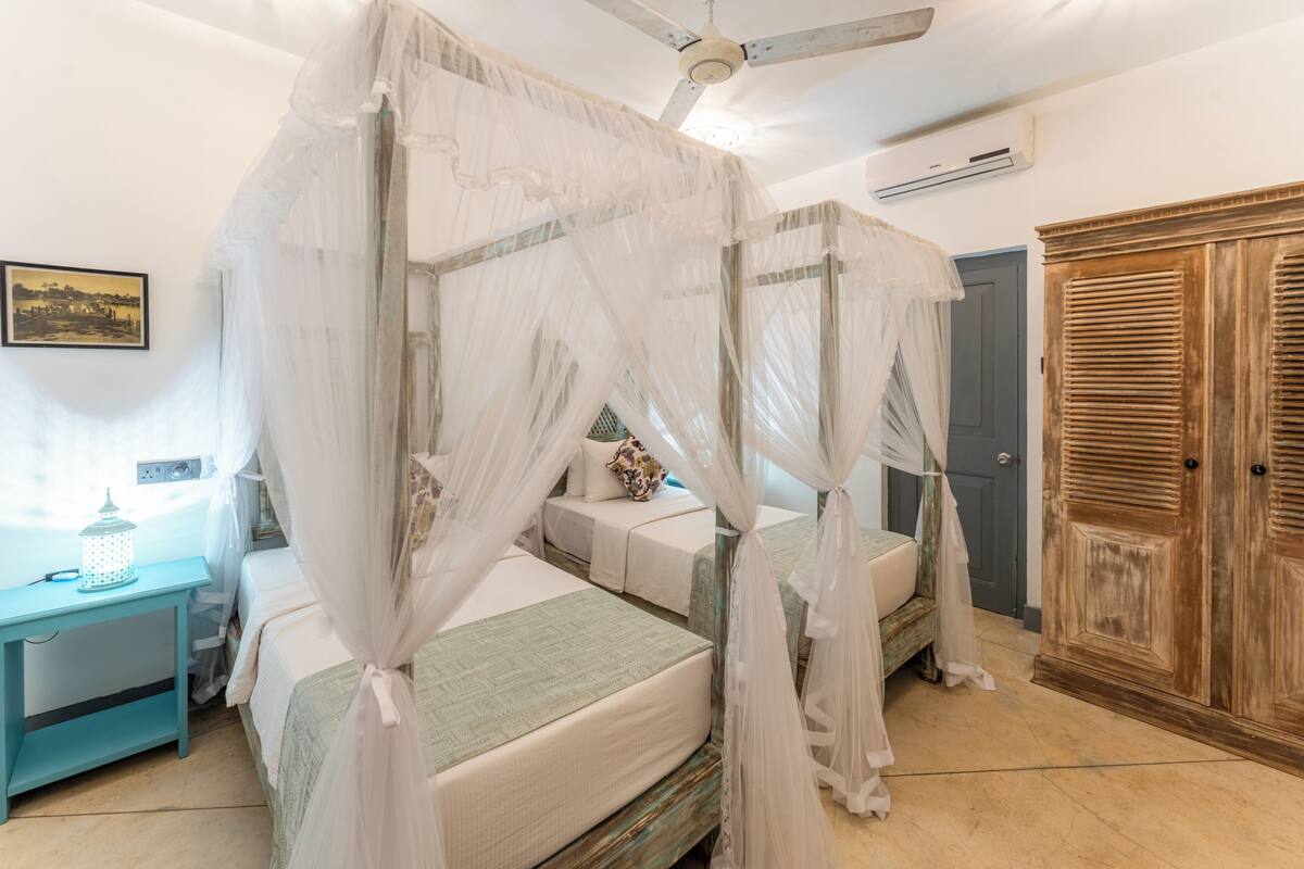 A four-poster canopy bed with a ceiling fan, a wooden wardrobe, and a small table with a lantern.