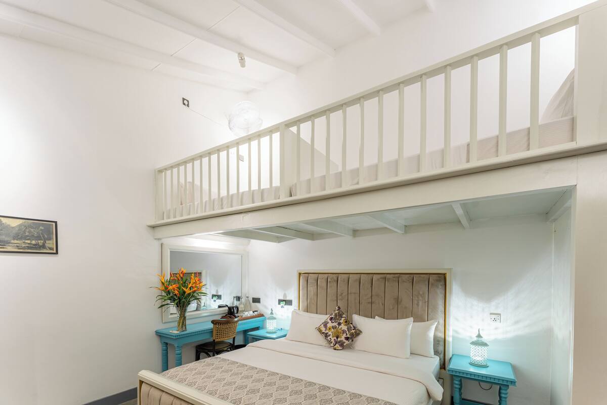 A room with a bed, a desk, a chair, a mirror, and a small table with a lantern.