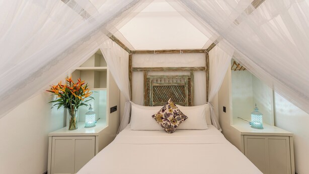 A bedroom with a canopy bed, a decorative headboard, bedside tables with lanterns, and a vase with flowers. - Parawa House (Galle)