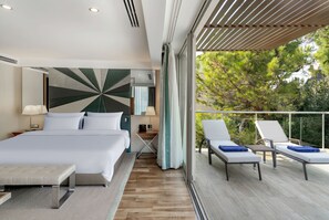 A modern hotel room with a large bed, a desk, and a balcony with lounge chairs.