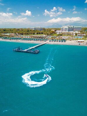 A coastal resort with a pier extending into turquoise waters, a sandy beach, and a backdrop of lush greenery and buildings.