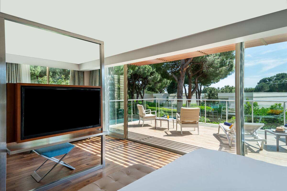 A modern balcony with a TV, seating, and a view of greenery.