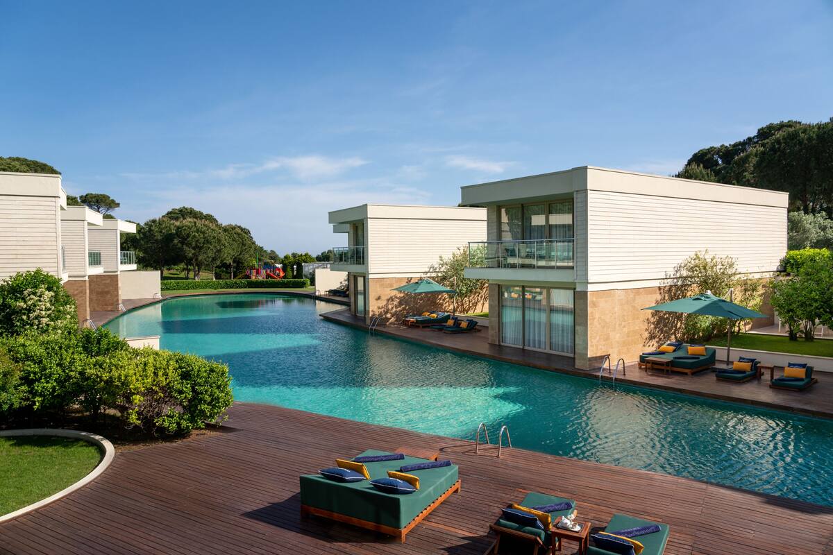 A modern hotel with a swimming pool, outdoor lounge area, and a view of the surrounding landscape.