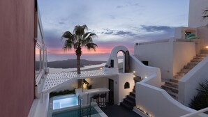 A modern pool area with a view of the sunset, a palm tree, and a staircase leading to a balcony. - Opera Mansion (Santorini)