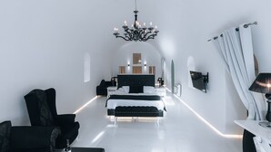 A modern bedroom with a large bed, a chandelier, and a white floor. - Opera Mansion (Santorini)